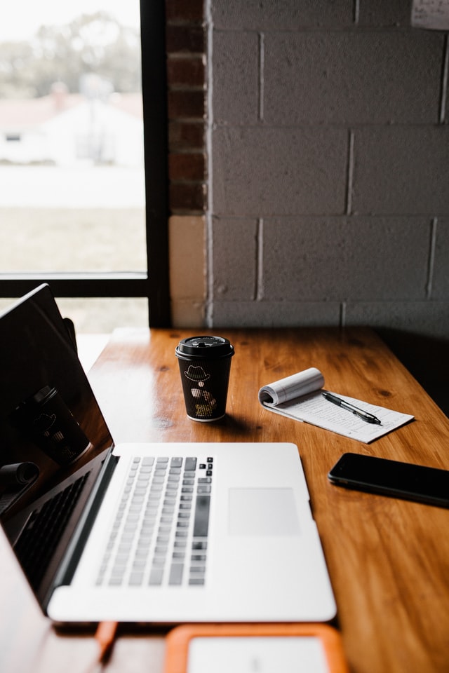 Open laptop next to a cup fo coffee, notebook and pen