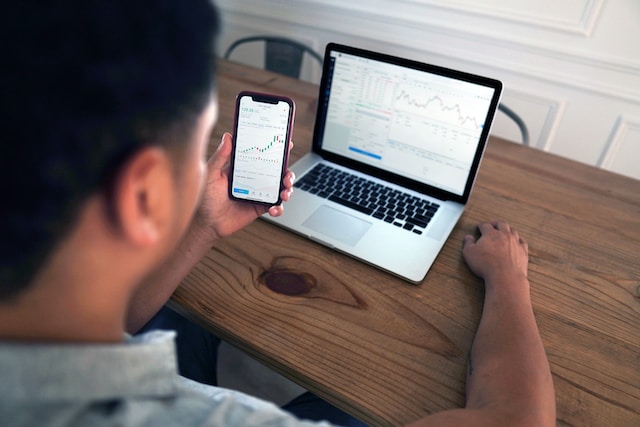 Man looking at stock charts on his phone and laptop