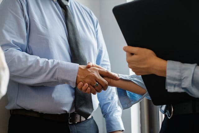 Two people (probably a man and a woman) shaking hands in what seems to be a business environment